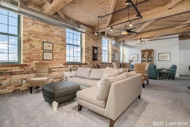 carpeted living room with rail lighting, brick wall, a high ceiling, and an inviting chandelier