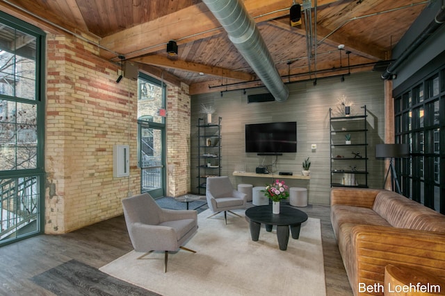 living area featuring brick wall, a high ceiling, wood finished floors, wood ceiling, and beam ceiling