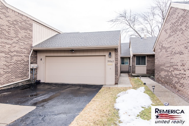 view of front facade featuring a garage, driveway, brick siding, and roof with shingles