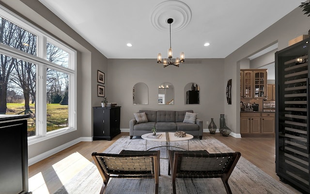 living area featuring a notable chandelier, baseboards, plenty of natural light, and light wood-type flooring