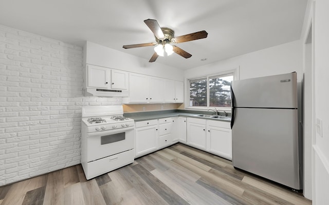 kitchen featuring freestanding refrigerator, white cabinets, under cabinet range hood, and white gas range