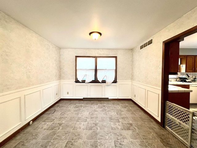 unfurnished room featuring a wainscoted wall, visible vents, and a decorative wall