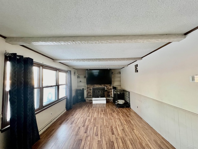 unfurnished living room with beam ceiling, wood finished floors, a textured ceiling, and wainscoting