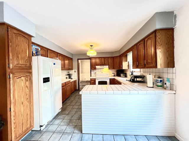 kitchen with white appliances, light tile patterned floors, decorative backsplash, tile countertops, and a peninsula