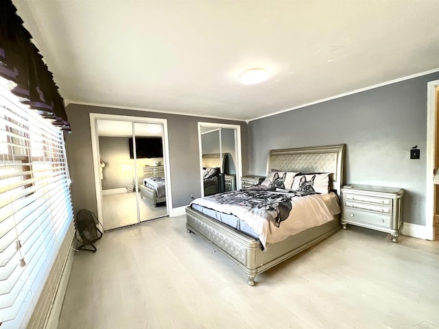 bedroom featuring ornamental molding, wood finished floors, baseboards, and two closets