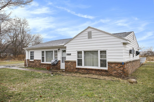 view of front of home featuring roof with shingles, a front yard, and brick siding