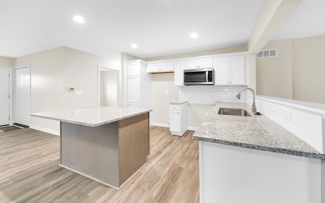 kitchen with light wood-style flooring, stainless steel microwave, visible vents, and white cabinetry