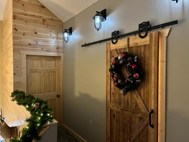 entryway with a barn door, wooden walls, and vaulted ceiling