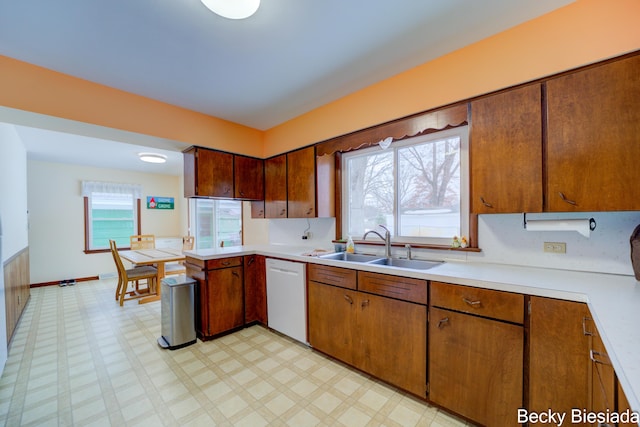 kitchen with brown cabinetry, dishwasher, light countertops, light floors, and a sink