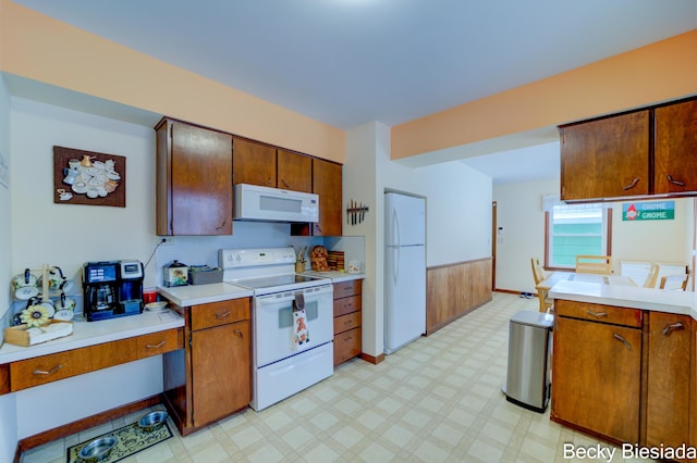 kitchen with white appliances, brown cabinetry, a wainscoted wall, light countertops, and light floors