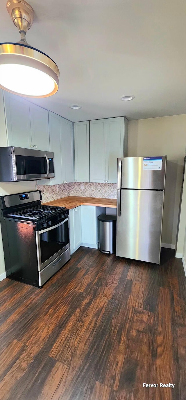 kitchen featuring dark wood-style flooring, stainless steel appliances, tasteful backsplash, butcher block counters, and baseboards