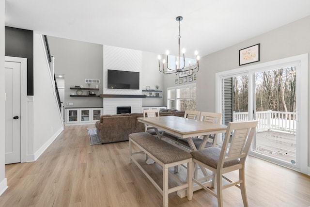 dining space with a chandelier, a fireplace, visible vents, baseboards, and light wood finished floors