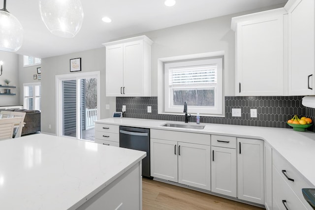 kitchen with light wood finished floors, tasteful backsplash, stainless steel dishwasher, white cabinetry, and a sink