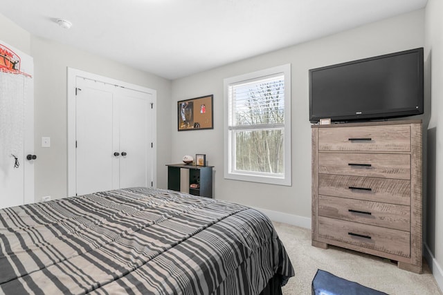 bedroom with baseboards, a closet, and light colored carpet