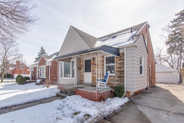 bungalow-style home featuring an outbuilding, a porch, a shingled roof, brick siding, and a detached garage