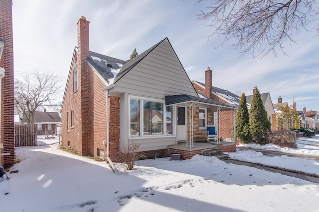 view of front of house with covered porch, brick siding, and a chimney