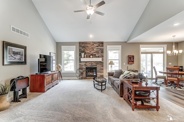 living room with high vaulted ceiling, light colored carpet, ceiling fan with notable chandelier, a fireplace, and visible vents