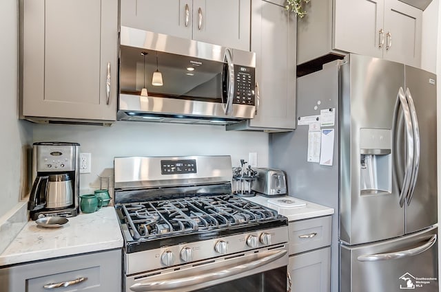 kitchen featuring a toaster, gray cabinets, light stone counters, and stainless steel appliances