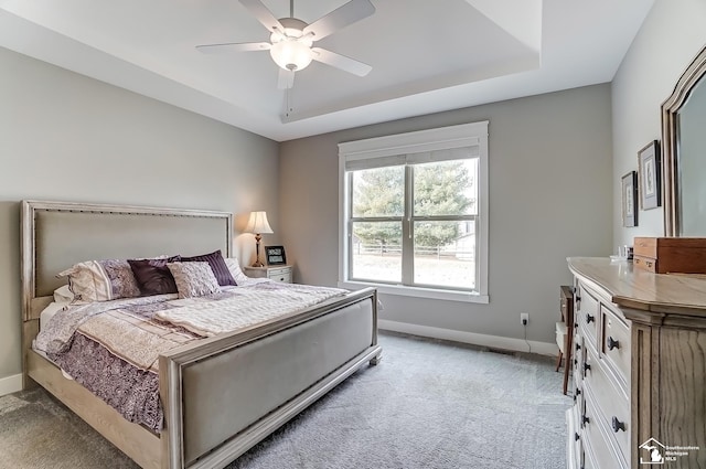 bedroom featuring a ceiling fan, a raised ceiling, light colored carpet, and baseboards