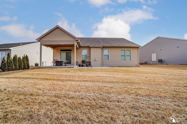 rear view of property with roof with shingles, a yard, and a patio