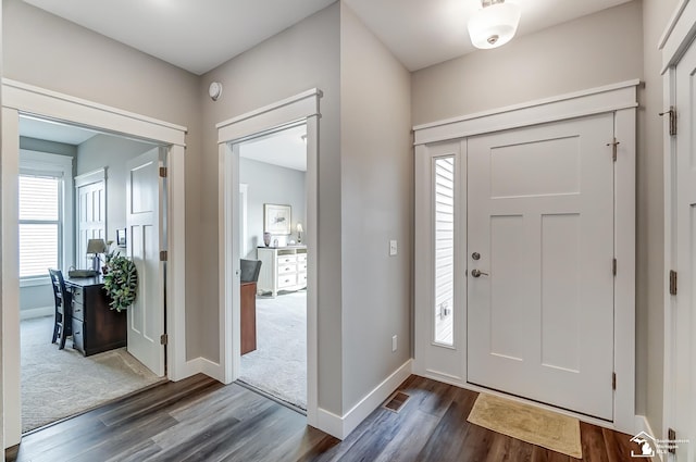 foyer entrance with dark wood-style floors, dark colored carpet, visible vents, and baseboards