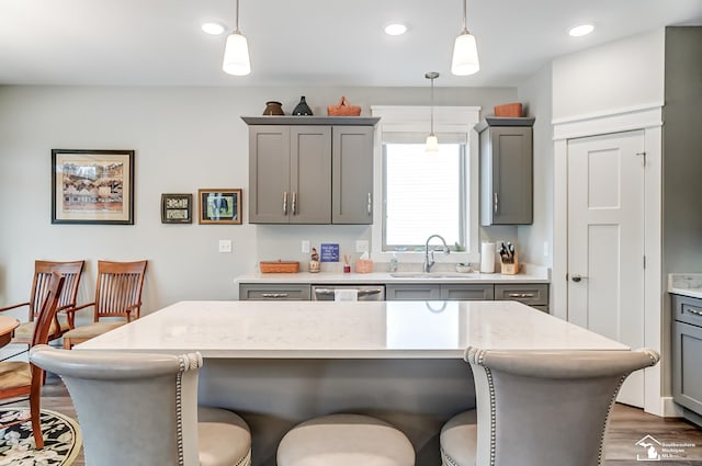 kitchen with a kitchen bar, a sink, hanging light fixtures, and gray cabinetry