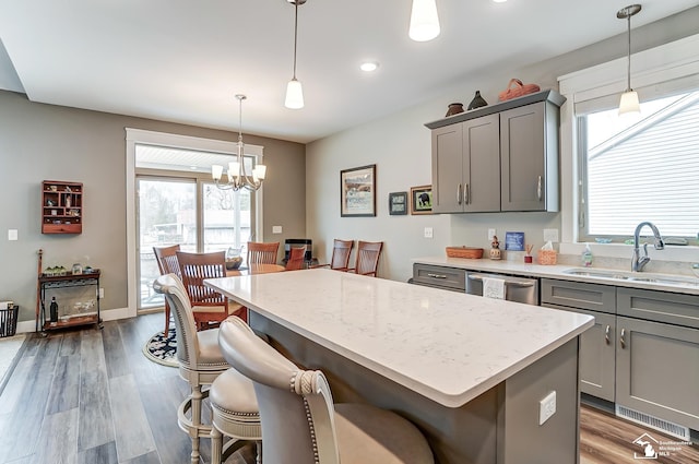 kitchen featuring gray cabinetry, wood finished floors, a sink, stainless steel dishwasher, and a center island