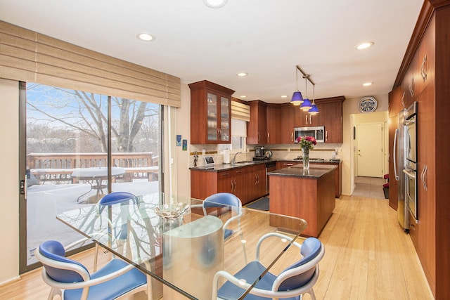 kitchen with stainless steel microwave, a kitchen island, glass insert cabinets, a sink, and light wood-type flooring
