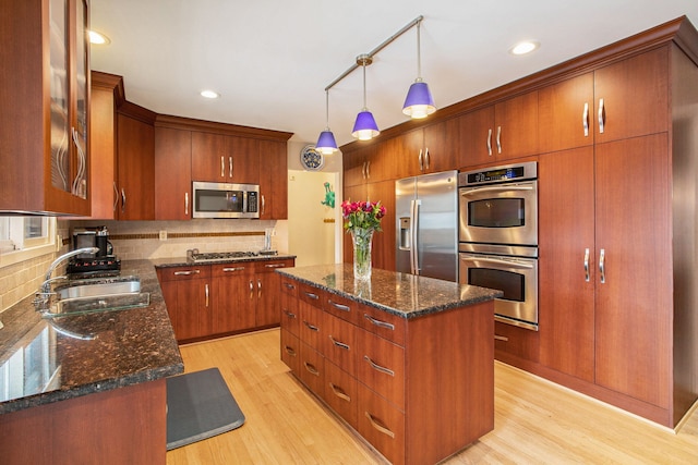 kitchen with a sink, stainless steel appliances, light wood finished floors, and decorative backsplash