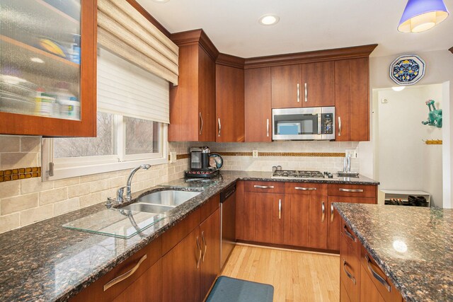 kitchen featuring dark stone counters, stainless steel appliances, a sink, light wood-type flooring, and backsplash