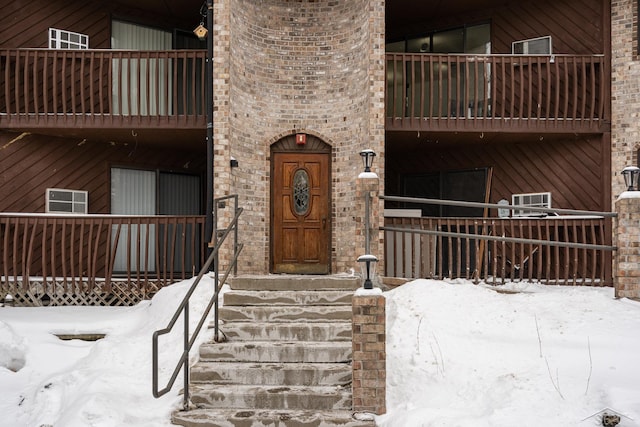 snow covered property entrance featuring a balcony and brick siding