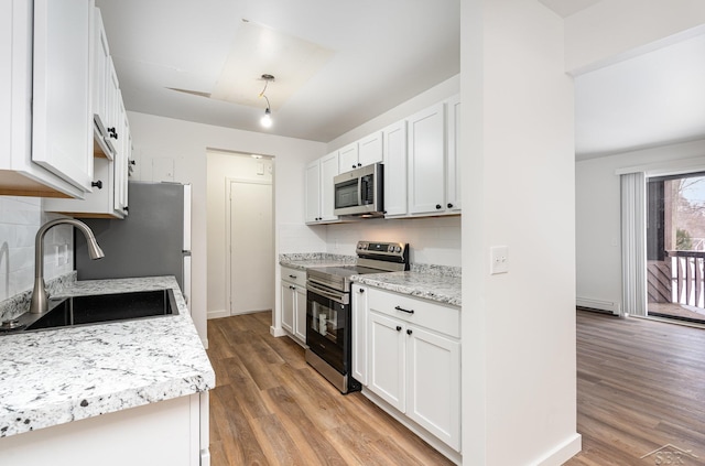 kitchen with stainless steel appliances, a baseboard radiator, decorative backsplash, a sink, and light wood-type flooring