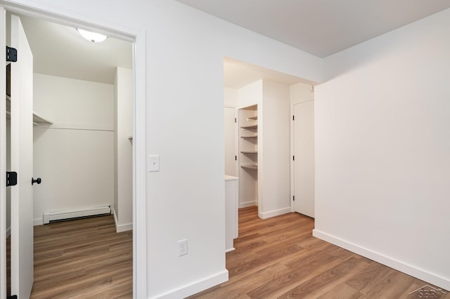 hall featuring baseboards, a baseboard heating unit, and wood finished floors