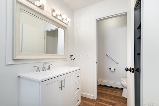 bathroom featuring a baseboard radiator, toilet, wood finished floors, vanity, and baseboards