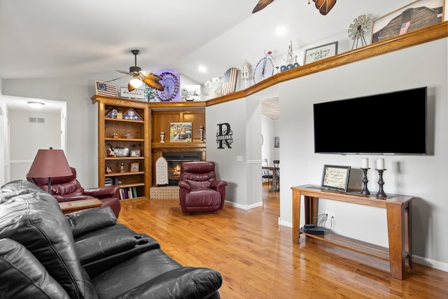 living area with a glass covered fireplace, wood finished floors, visible vents, and ceiling fan