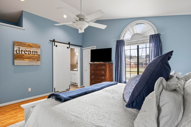 bedroom with wood finished floors, baseboards, ceiling fan, a barn door, and connected bathroom