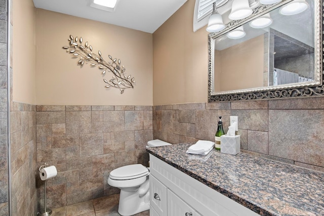 full bath with tile patterned flooring, a wainscoted wall, toilet, vanity, and tile walls