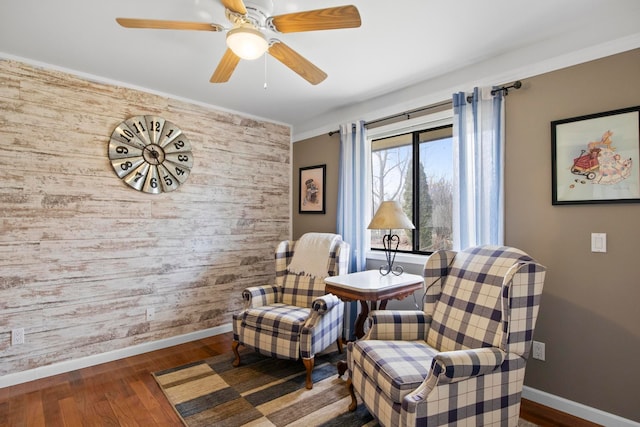 living area with a ceiling fan, an accent wall, baseboards, and wood finished floors