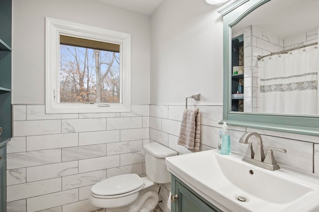 bathroom with toilet, vanity, wainscoting, a shower with curtain, and tile walls