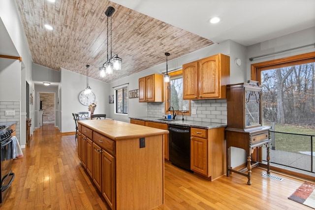 kitchen featuring a sink, black appliances, light wood-style floors, backsplash, and a center island