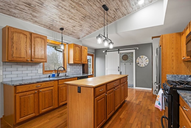 kitchen with a sink, black appliances, a barn door, brown cabinets, and a center island