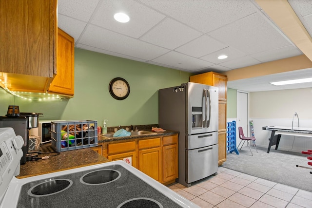 kitchen featuring a sink, stainless steel refrigerator with ice dispenser, light carpet, dark countertops, and brown cabinets