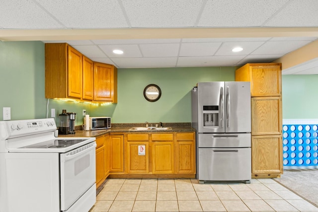 kitchen featuring light tile patterned floors, brown cabinetry, a sink, appliances with stainless steel finishes, and dark countertops