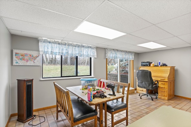 dining space featuring light tile patterned flooring, a paneled ceiling, and baseboards