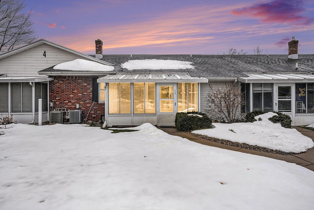 snow covered house featuring brick siding, a chimney, and a sunroom