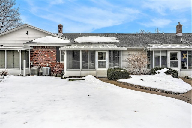 snow covered rear of property featuring brick siding, a chimney, and a sunroom