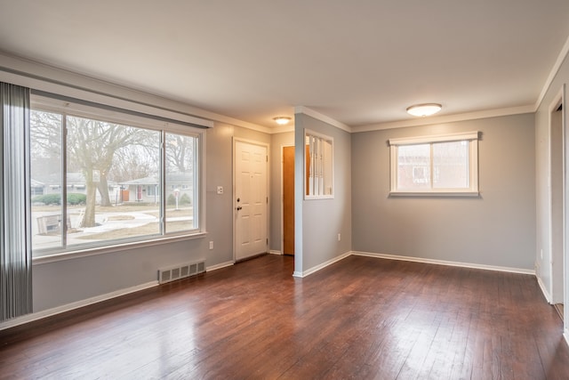 empty room with dark wood-type flooring, visible vents, ornamental molding, and baseboards