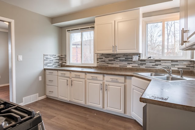 kitchen with visible vents, decorative backsplash, white cabinets, a sink, and wood finished floors