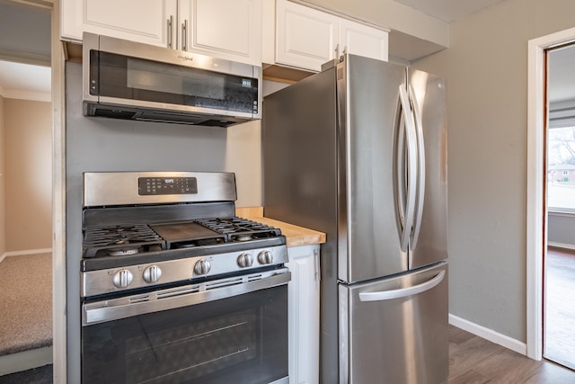 kitchen with wood finished floors, baseboards, white cabinets, light countertops, and appliances with stainless steel finishes