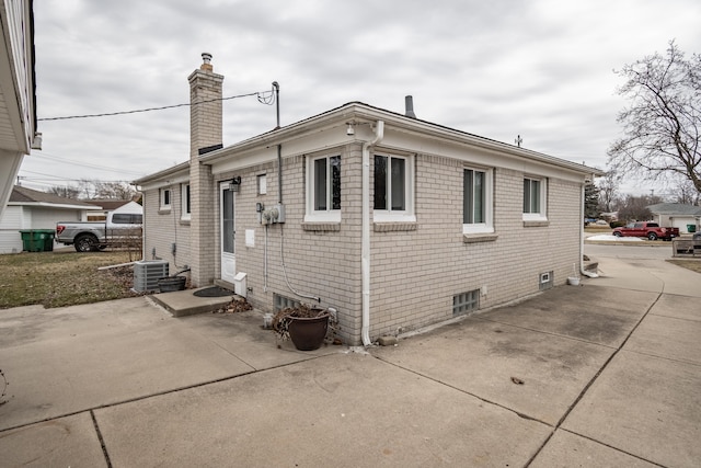 rear view of house with entry steps, a chimney, cooling unit, and brick siding